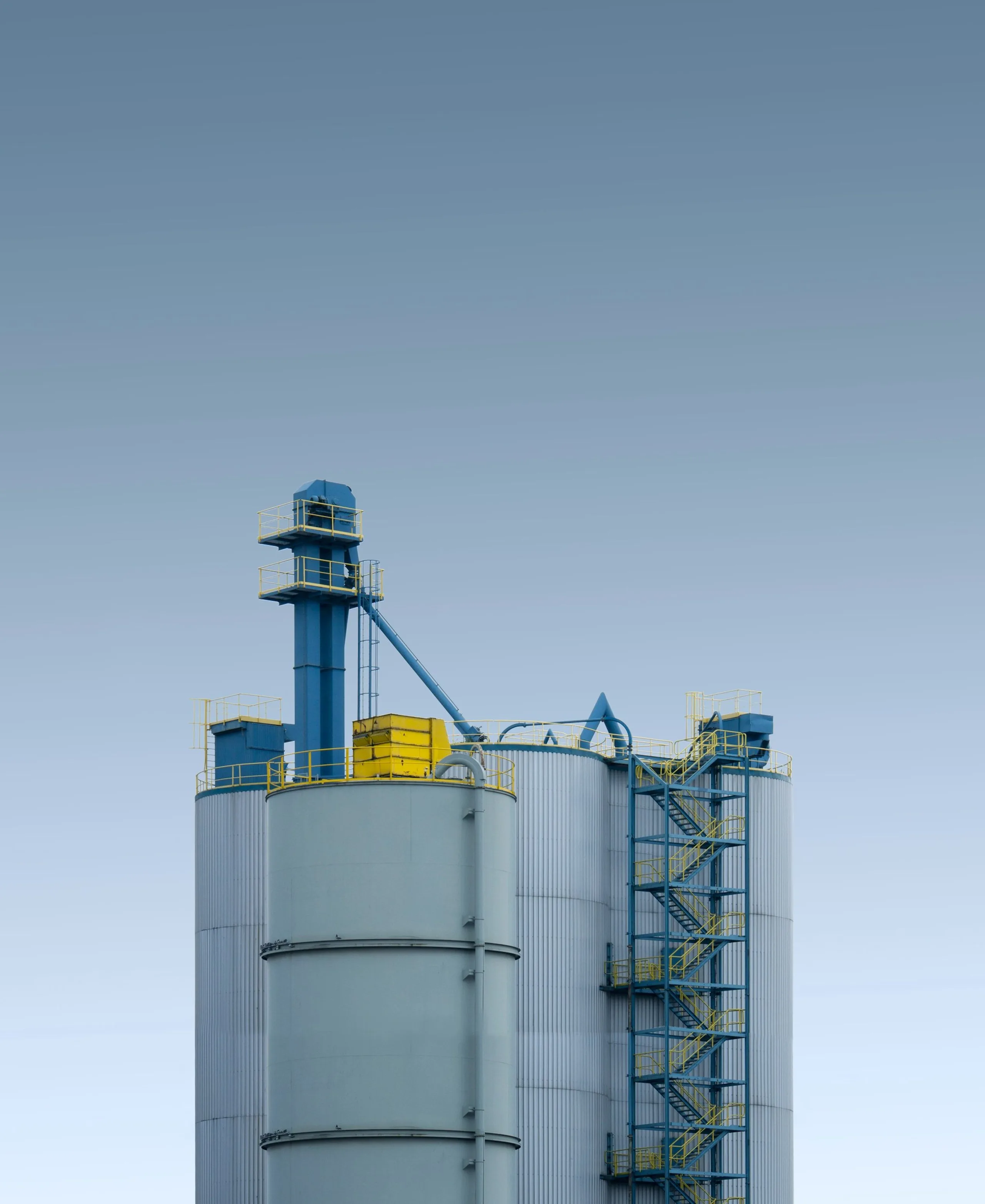 Bulk storage silo tower with a blue bucket elevator against a clear sky.