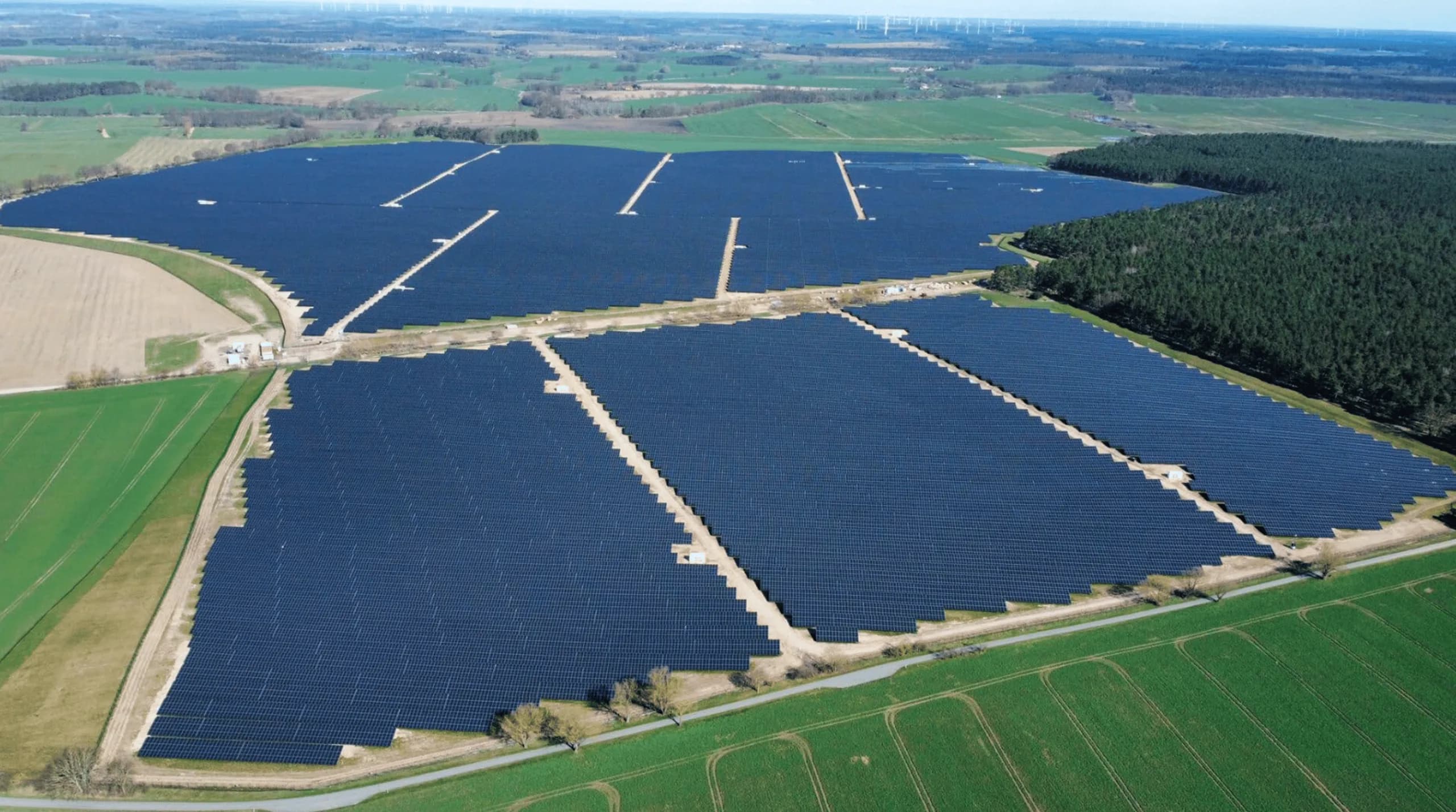 Aerial view of a ground-mounted solar park set between farmland and forest.