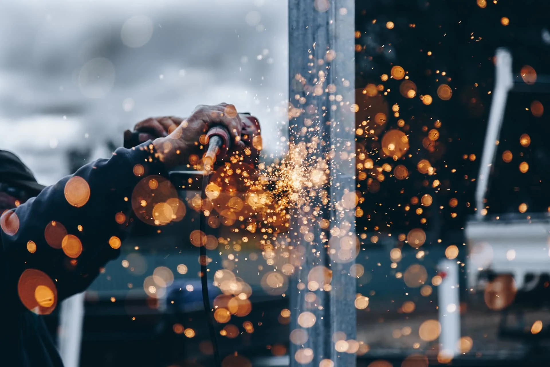 Worker grinding a steel column, sparks scattering across the frame.